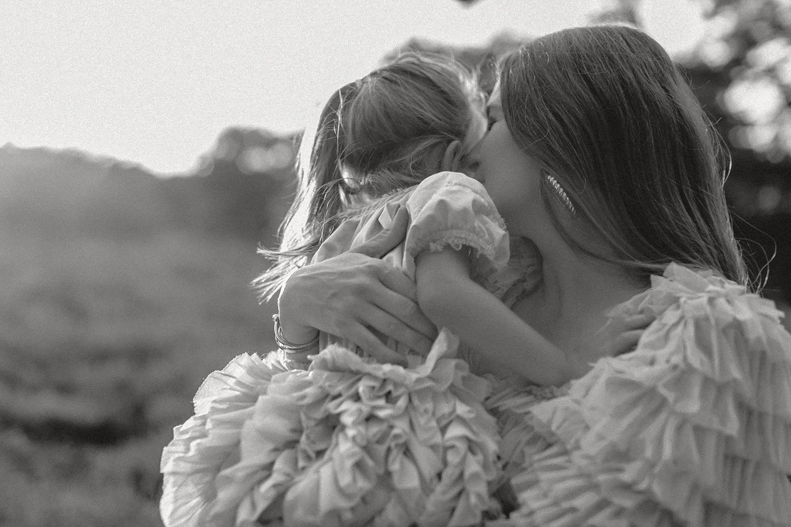 Zwei Frauen umarmen sich und küssen sich draußen bei Sonnenuntergang, verloren in einem emotionalen Moment.