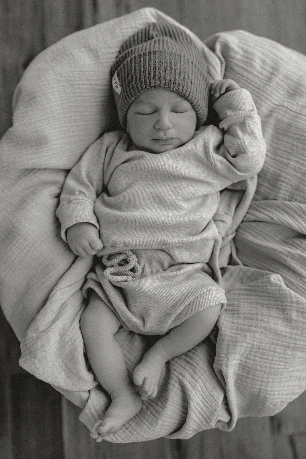 Ein schlafender Neugeborener in Kleidung und einer Mütze, liegend auf einer weichen Decke.