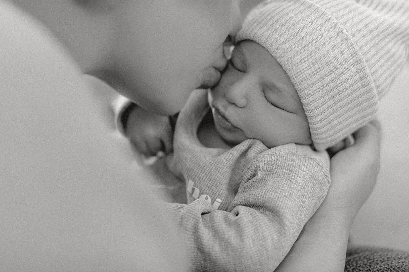 Ein Baby liegt schlafend in den Händen einer Person, trägt einen gestrickten Hut und einen Pullover.