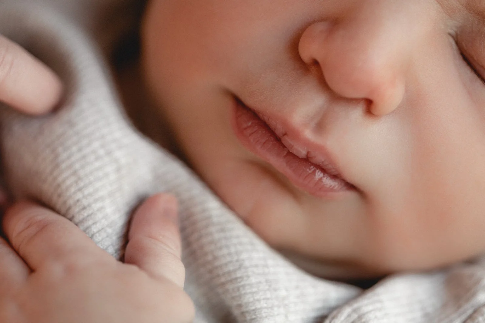 Nahaufnahme eines schlafenden Babys mit geschlossenen Augen, das einen weichen, hellgrauen Pullover trägt.