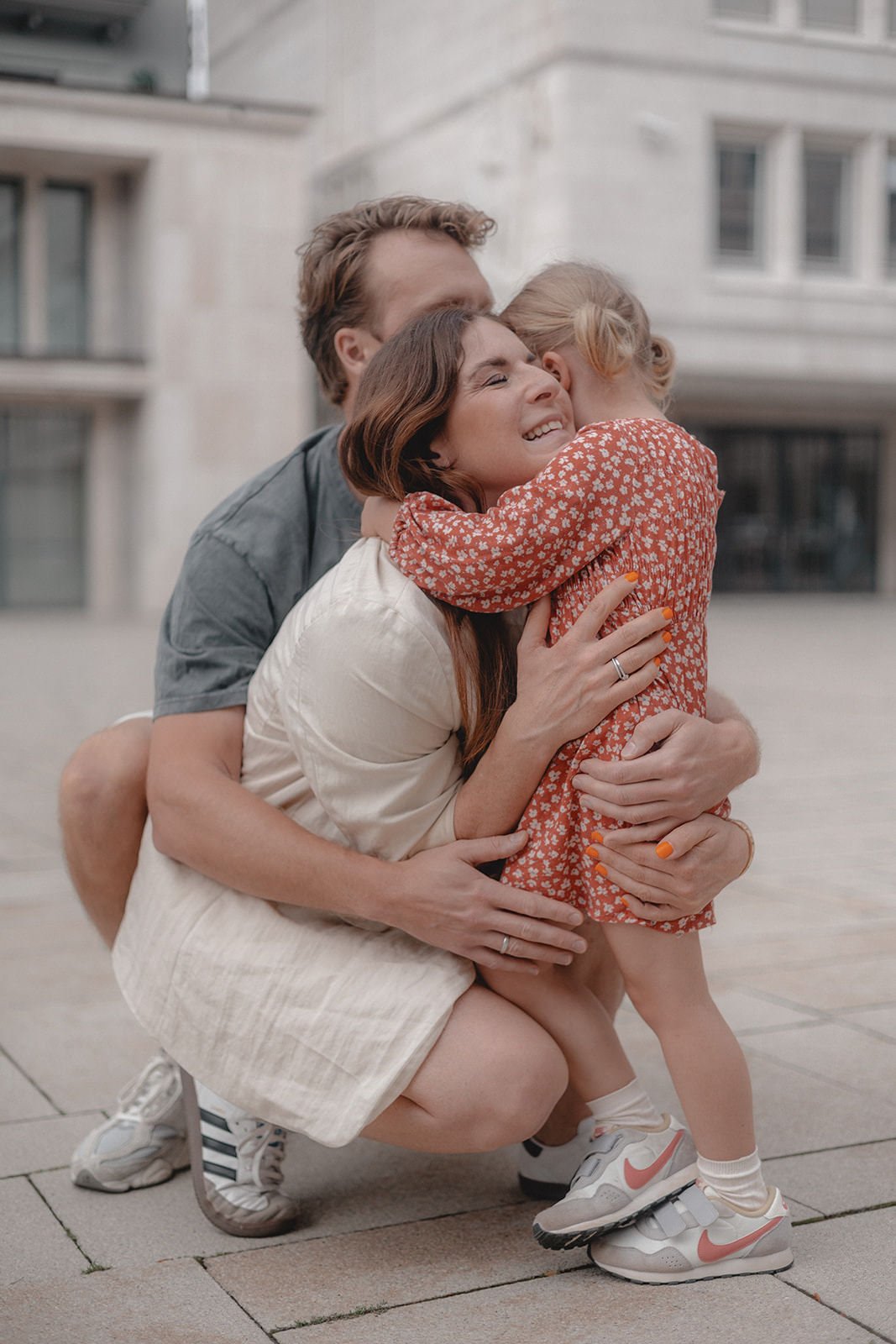 Familie umarmt sich lachend auf der Straße vor einem Gebäude.