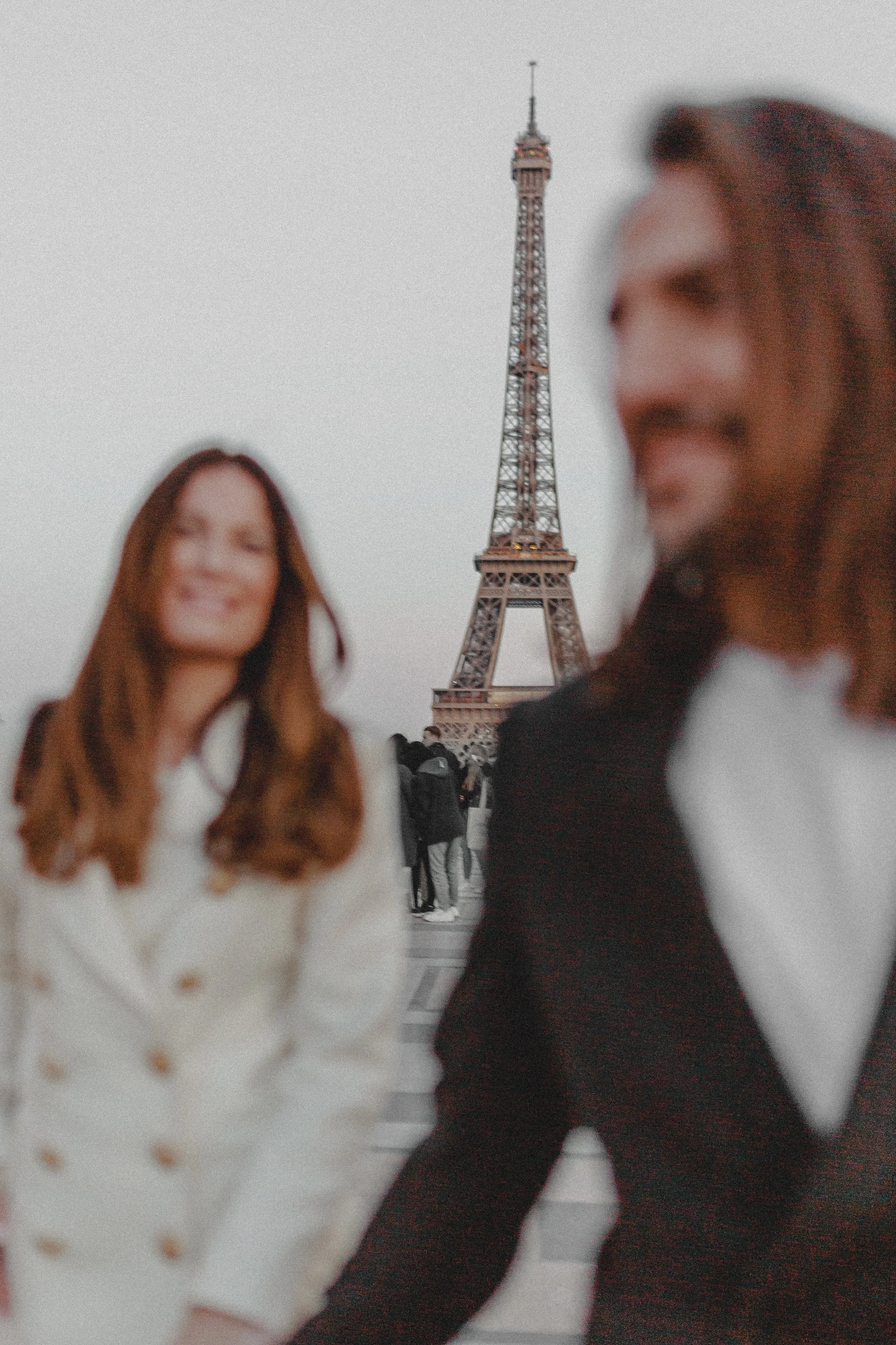 Zwei Menschen in der Nähe des Eiffelturms in Paris, sind unscharf und lächeln, im Hintergrund ist der Eiffelturm zu sehen.