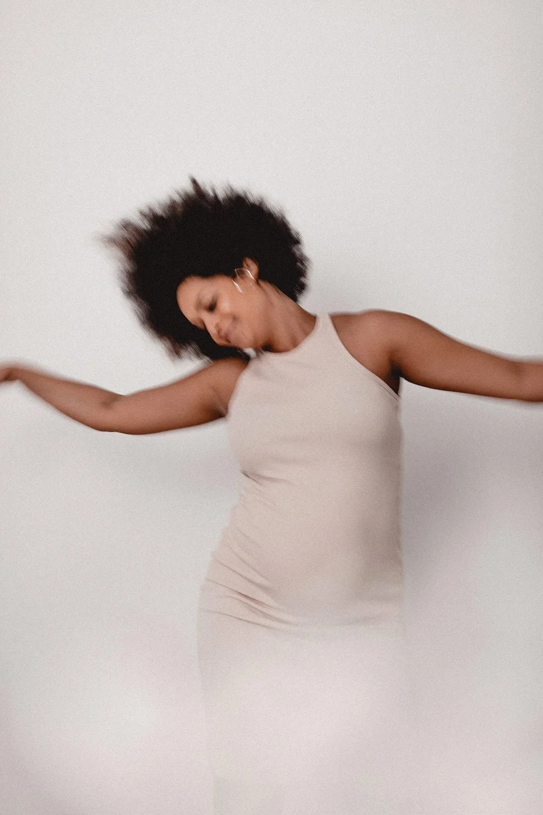 Frau mit Afro-Haar, die in einem weißen Kleid tanzt, mit einem neutralen Hintergrund.