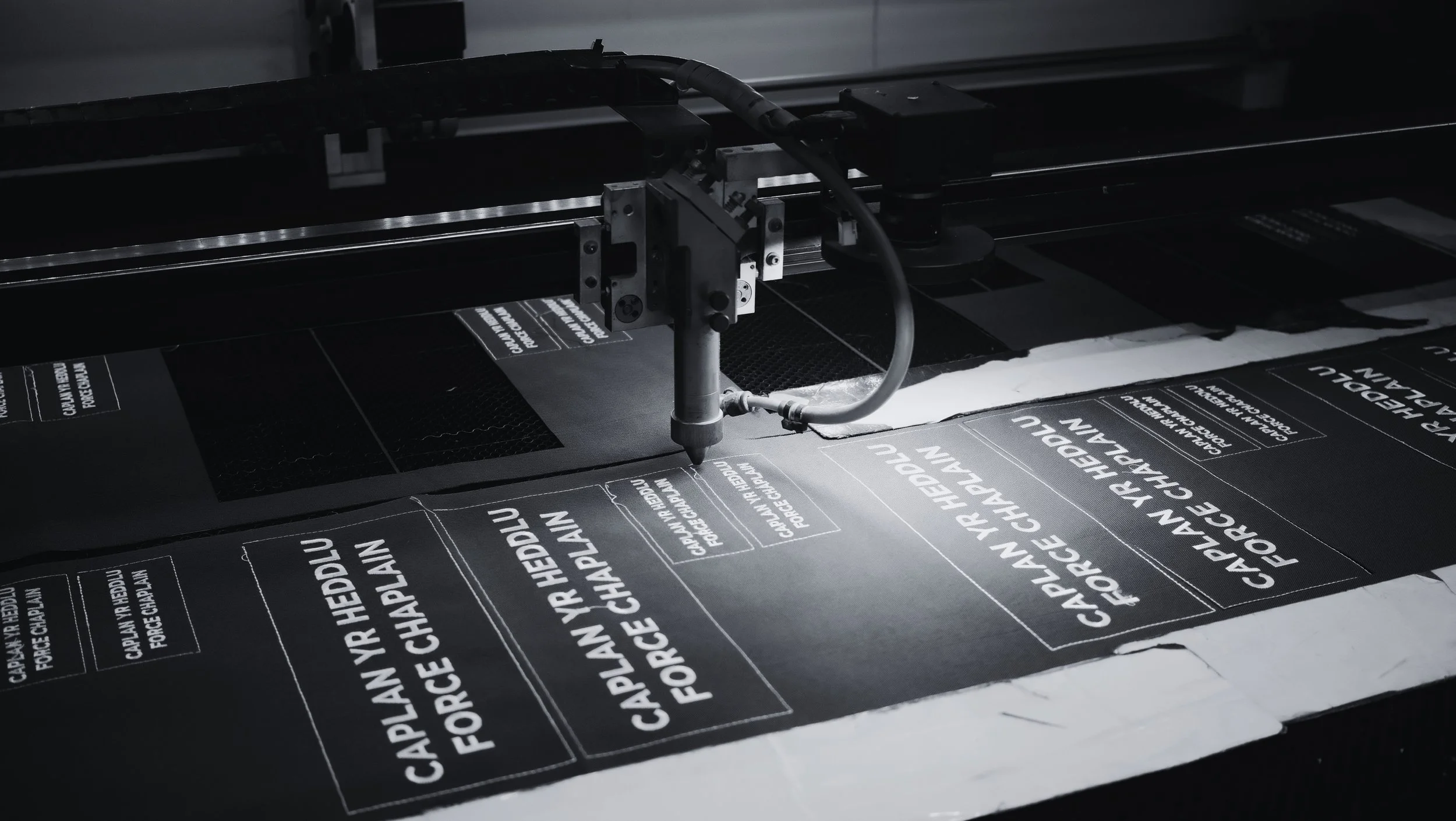 A large industrial printer printing black stickers with white text that say "CAPTAIN VR HEADLU FORCE CHAPLAIN".