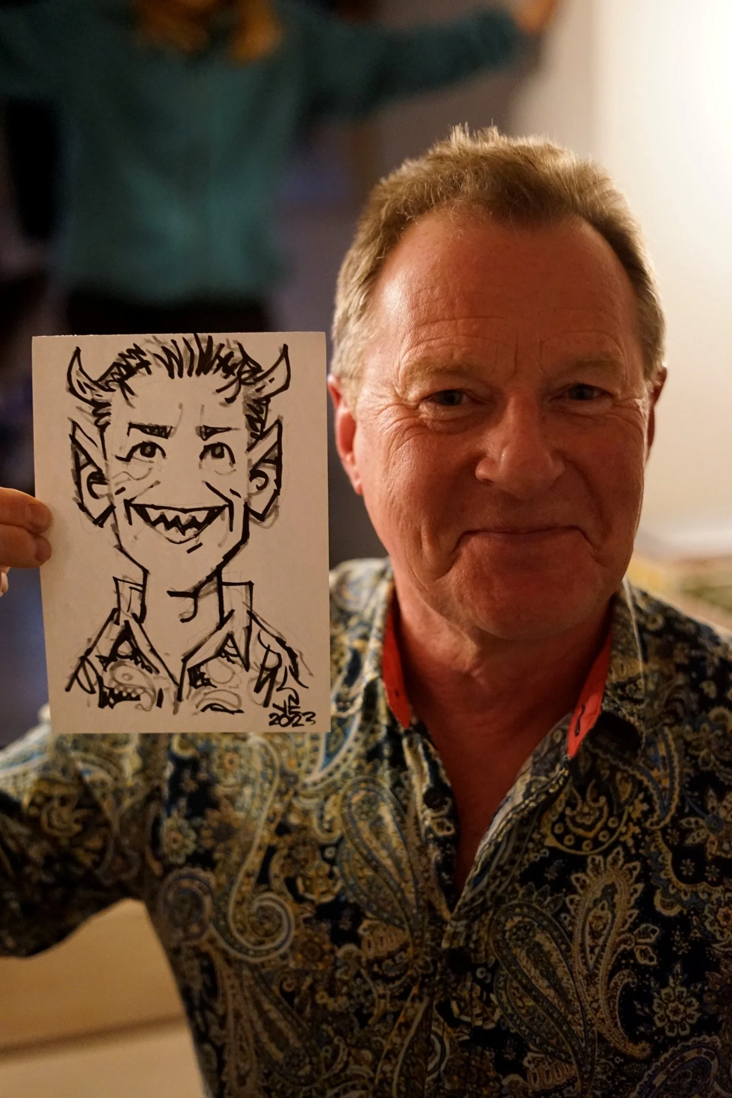 Man holding a drawing of a cartoon devil character with horns, sharp teeth, and a mischievous smile.