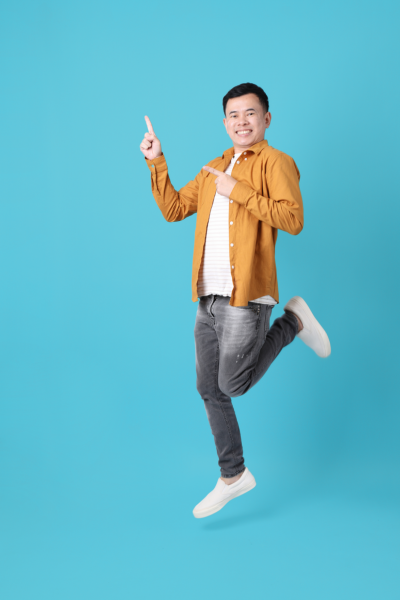 Homme souriant sautant avec le doigt levé, portant un style décontracté, contre un fond bleu