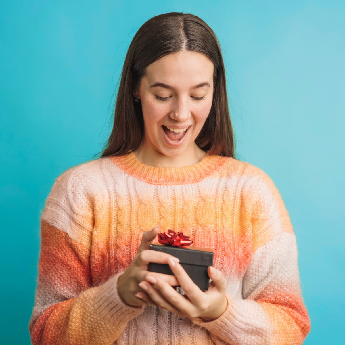 Une femme souriante examine un petit cadeau avec un ruban rouge un soir de fête.