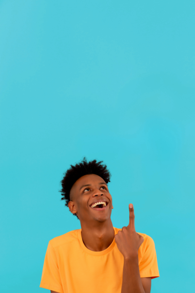 Une jeune personne souriante portant un t-shirt jaune, pointant vers le haut avec le doigt contre un fond bleu.