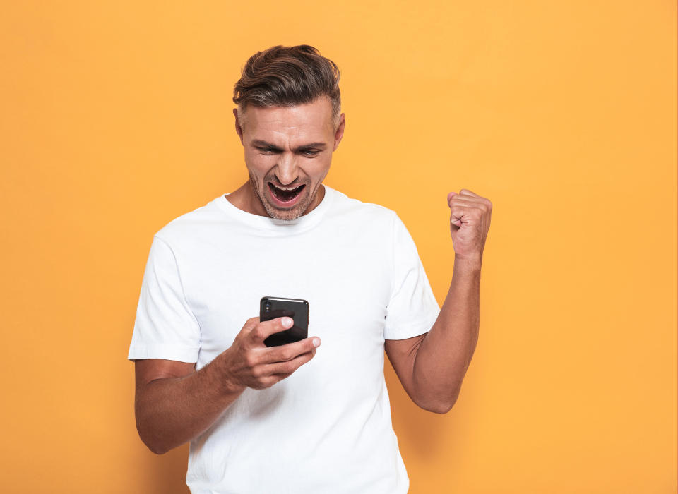 Homme souriant avec poing levé regardant son téléphone contre un fond jaune
