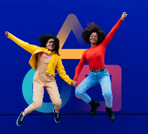 Deux femmes joyeuses avec des cheveux bouclés sautent en tenant la main devant un mur bleu avec des formes géométriques colorées. L'une porte un pull rouge et un jean, l'autre une veste jaune et un pantalon beige.