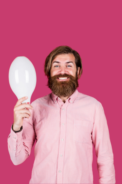 Homme souriant tenant un ballon blanc, portant une chemise rose clair, sur un fond rose