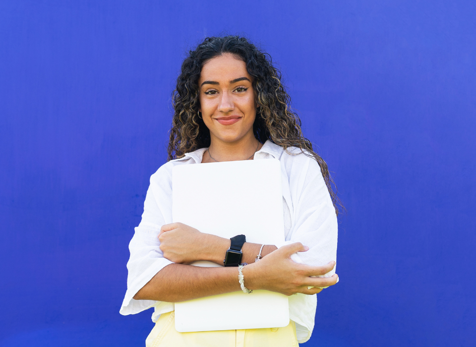 Jeune femme souriante tenant un ordinateur portable blanc contre un mur bleu.