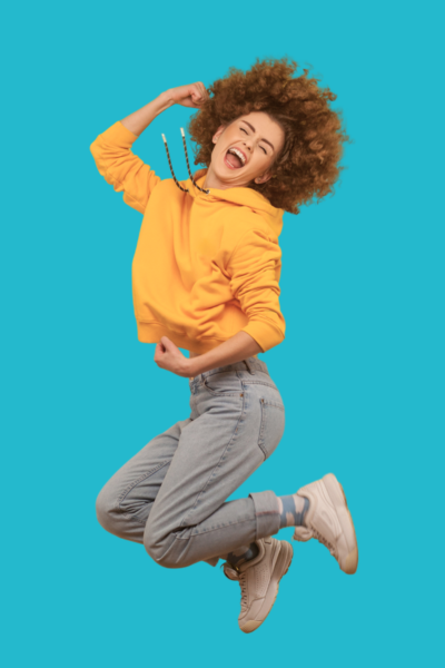 Jeune femme joyeuse sautant en l'air avec un hoodie jaune contre un fond bleu.