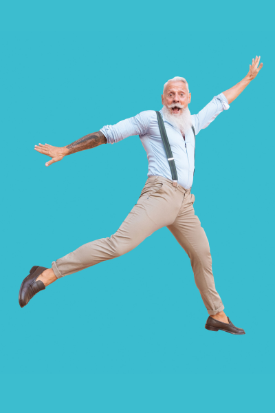 Un homme âgé souriant en pantalon beige, chemise bleue, with suspenders, sautant de joie contre un fond bleu.
