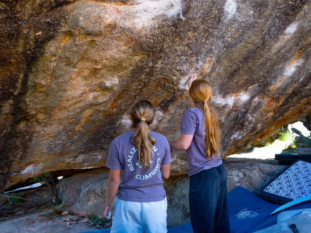 Two athletes studying the holds on an overhanging boulder before an attempt