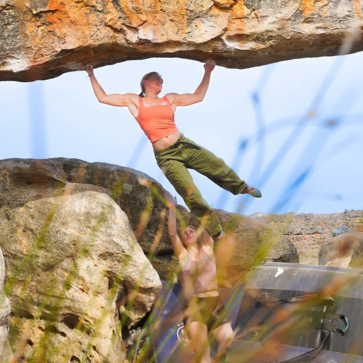 An athlete hanging from the lip of a sandstone roof against the sky