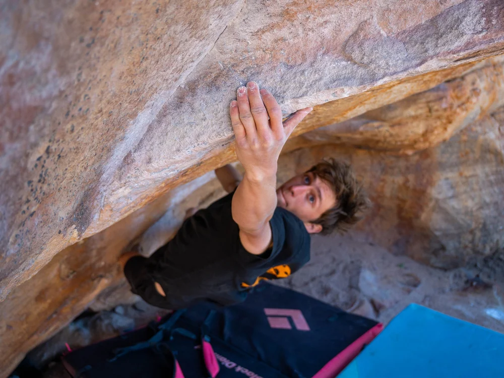 An athlete pulling through a steep sandstone roof above the crash pads