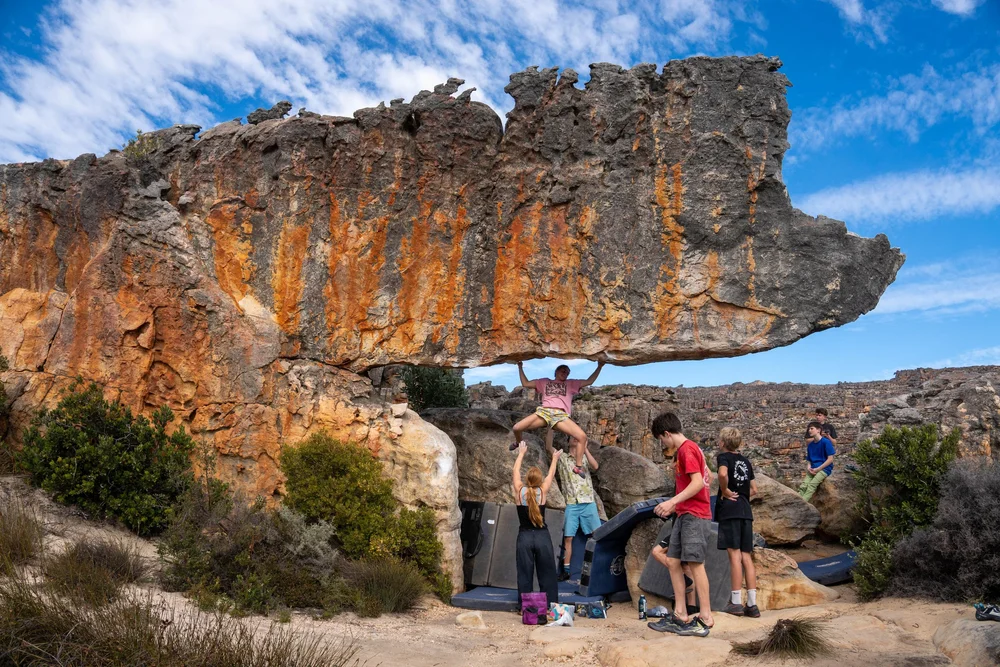 A teen climber under the Rhino roof in Rocklands while teammates spot below