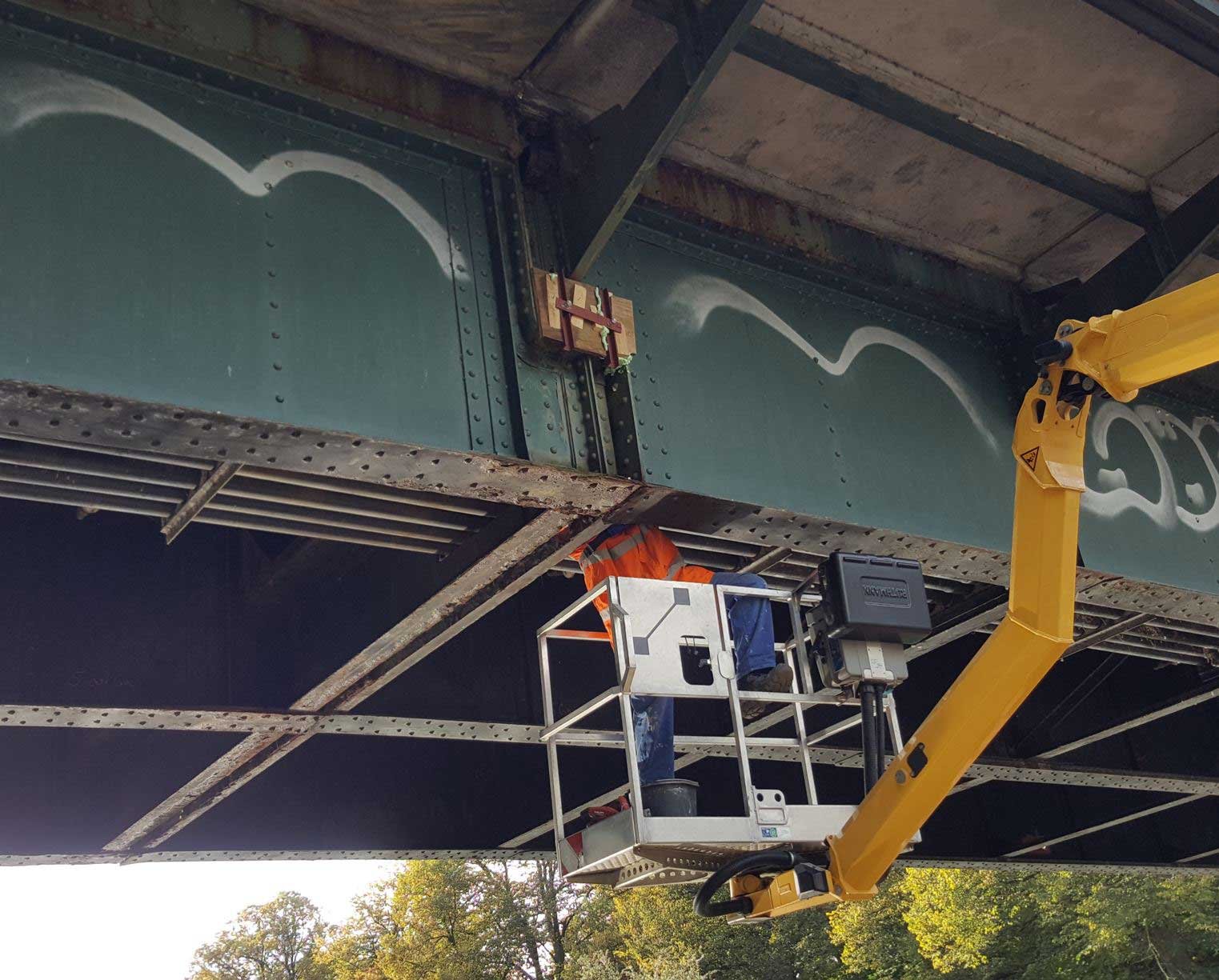 Brückensanierung unter laufendem Betrieb mit Arbeitsbühne – Ingenieure und Bauarbeiter bei Instandsetzungsarbeiten an Stahlkonstruktion in Lübeck.