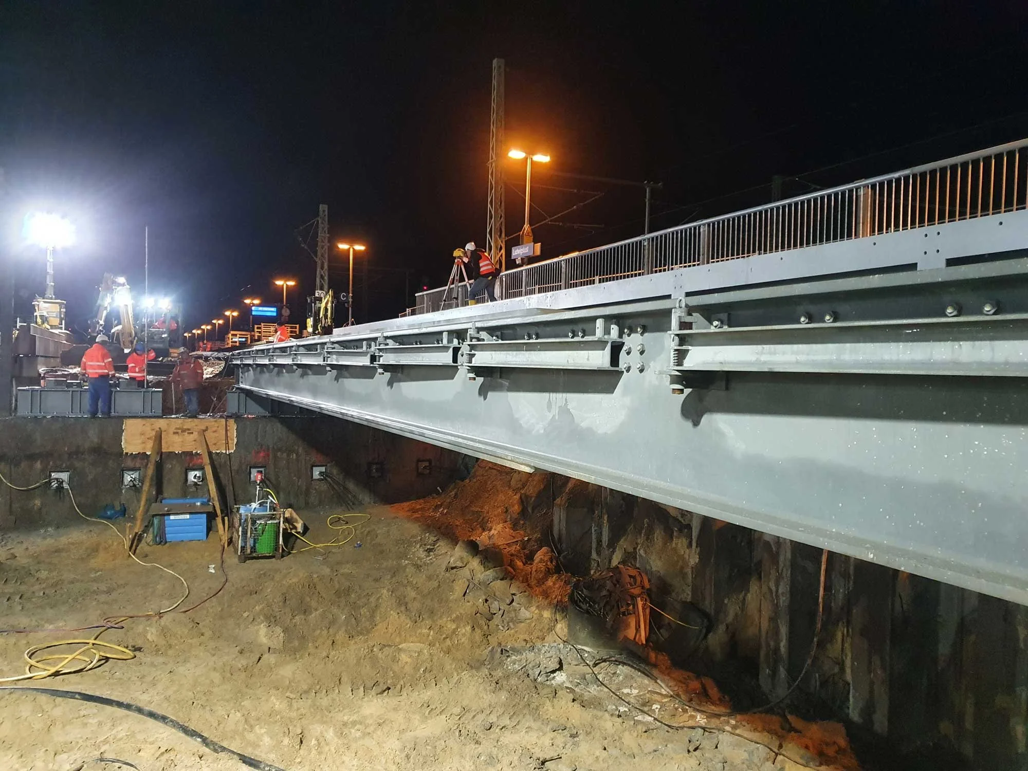 Brückenbau bei Nacht in Ludwigslust: Bauarbeiter und Ingenieure beim Einmessen einer Stahlbrücke auf einer beleuchteten Baustelle in Mecklenburg-Vorpommern.