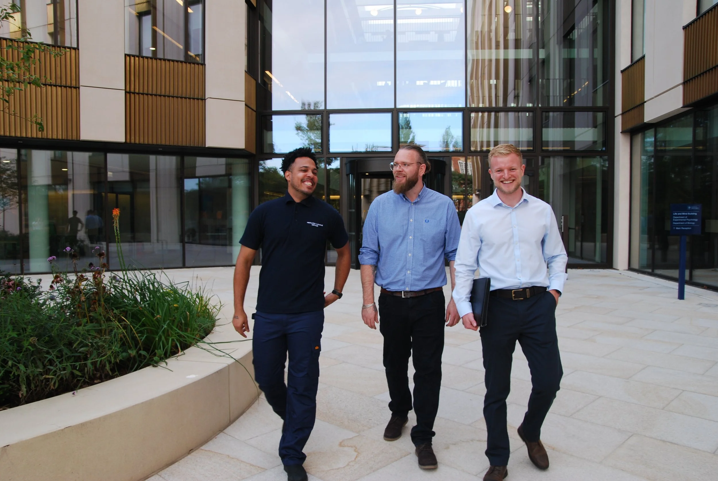 Three men walking outside a modern office building, smiling and engaging in conversation.