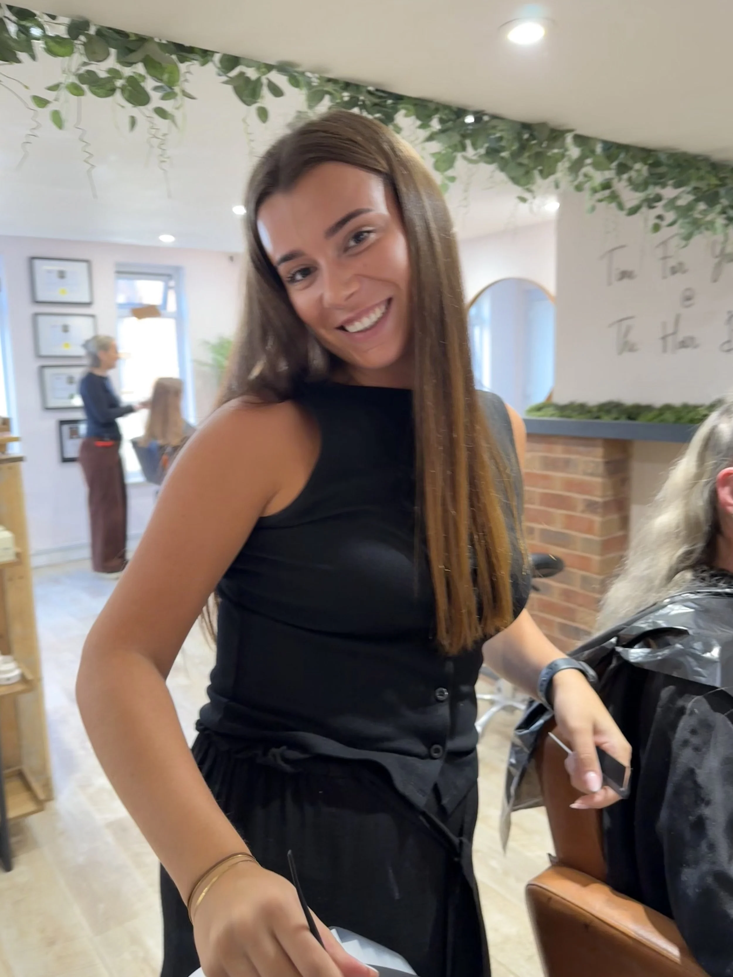 A woman with sunglasses smiling outdoors near lush green tropical plants, with the text '*CURRENTLY TRAVELLING*' overlayed.