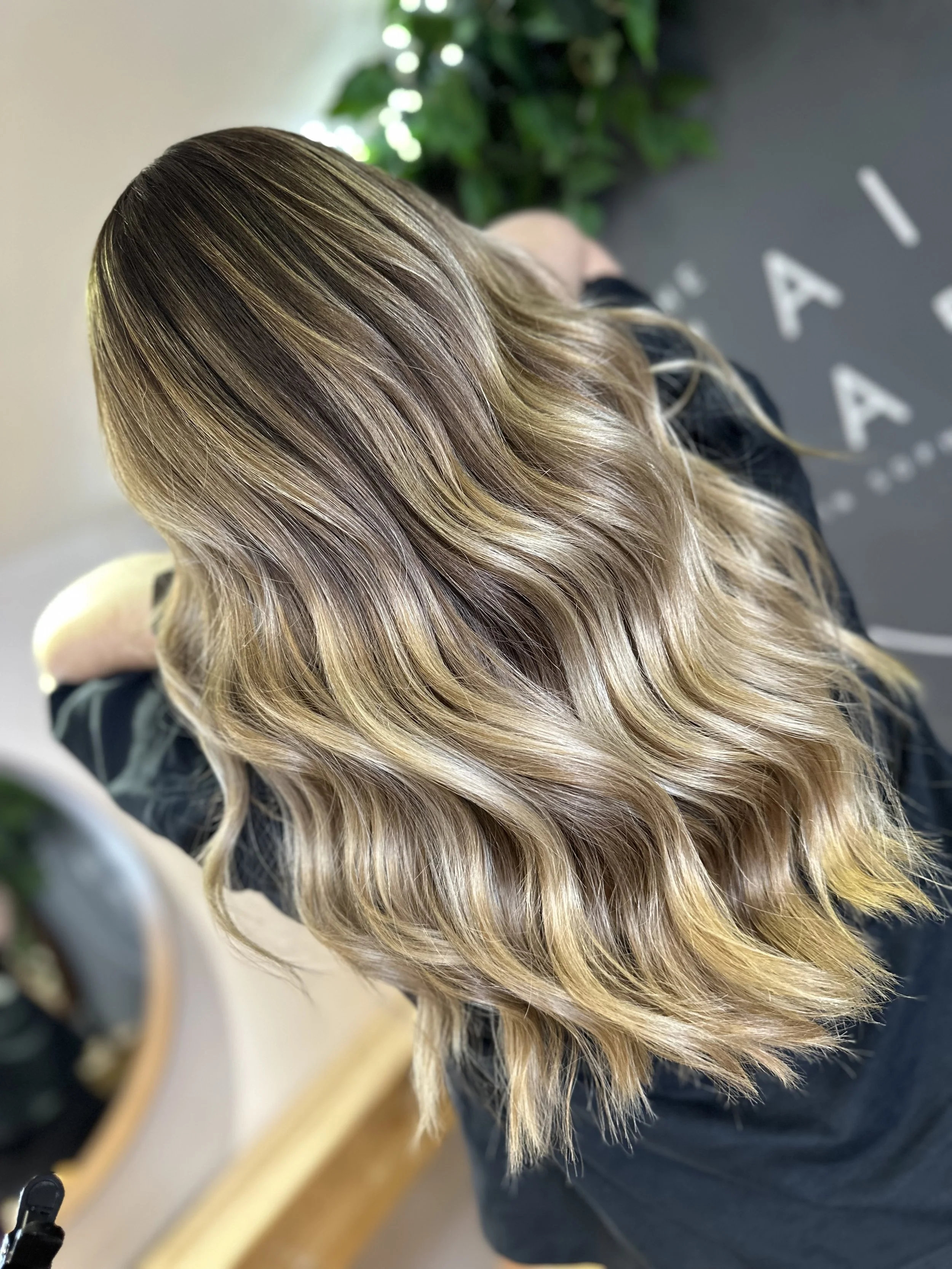 Woman with long, wavy, blonde hair, sitting in a salon.