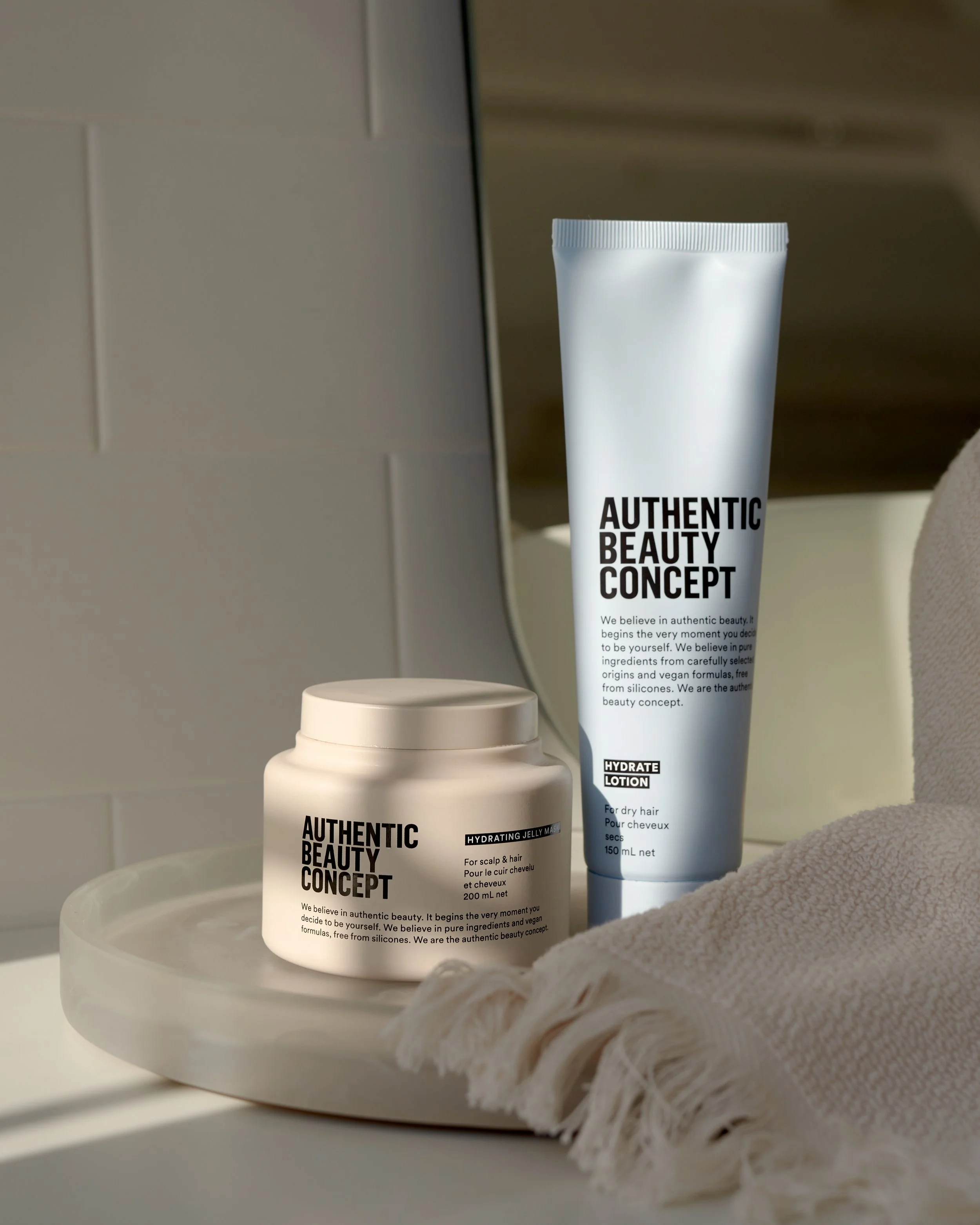 Skincare products labeled 'Authentic Beauty Concept' on a tray, with a towel and mirror reflection in the background.