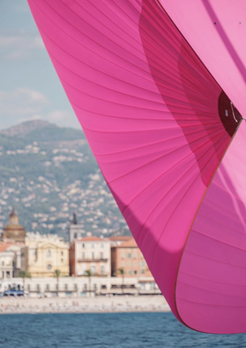 Un parasol rose vif avec une ville en arrière-plan, située près de la mer, avec des montagnes en fond.