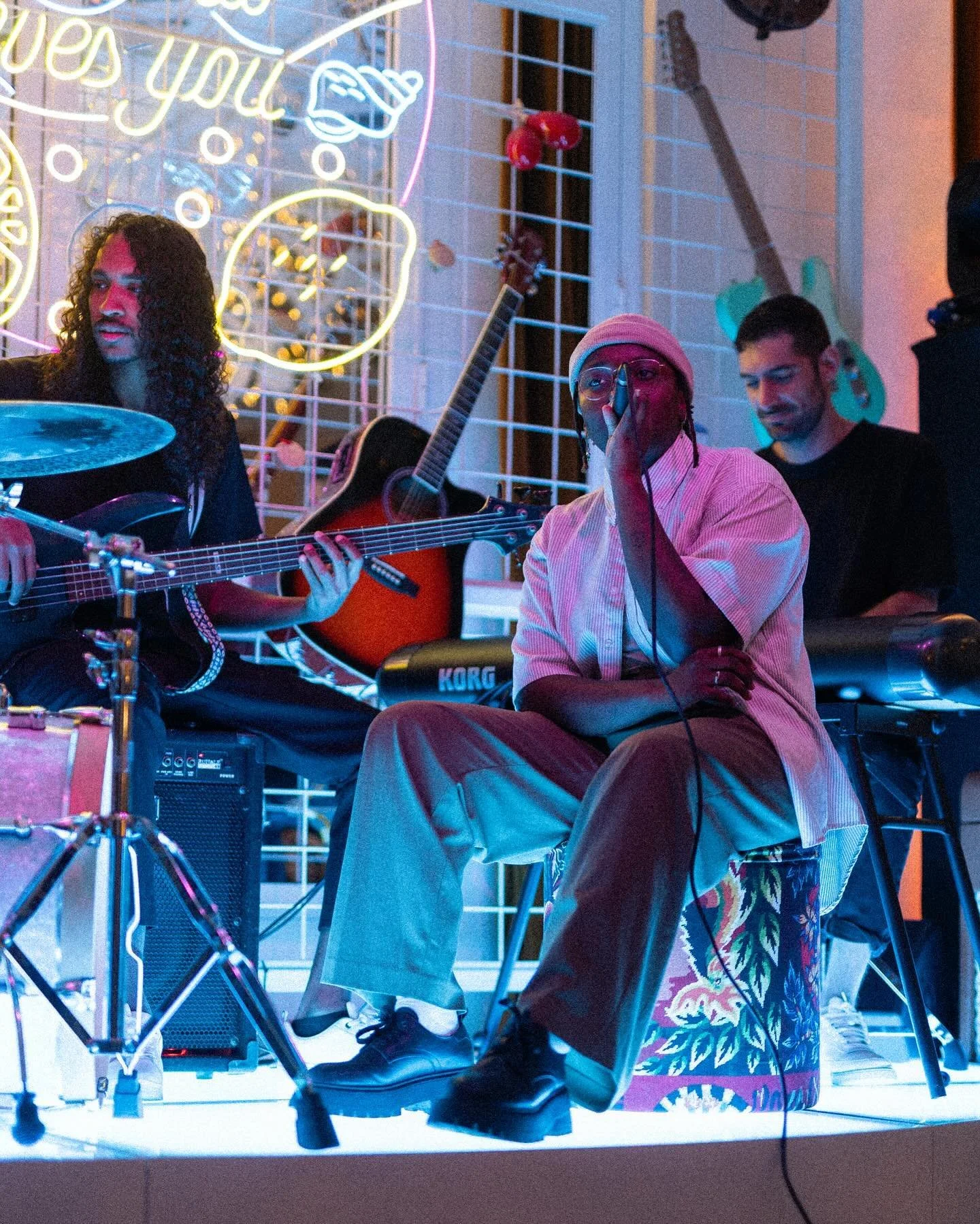 Un groupe de musiciens jouant lors d'une performance dans un lieu coloré avec des guitares, psychédélique, neon, et un piano, ambiance intime et artistique.