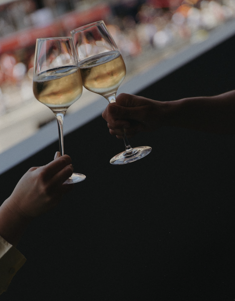 Deux personnes toastent avec des verres de vin blanc à fond sombre, en arrière-plan flou.