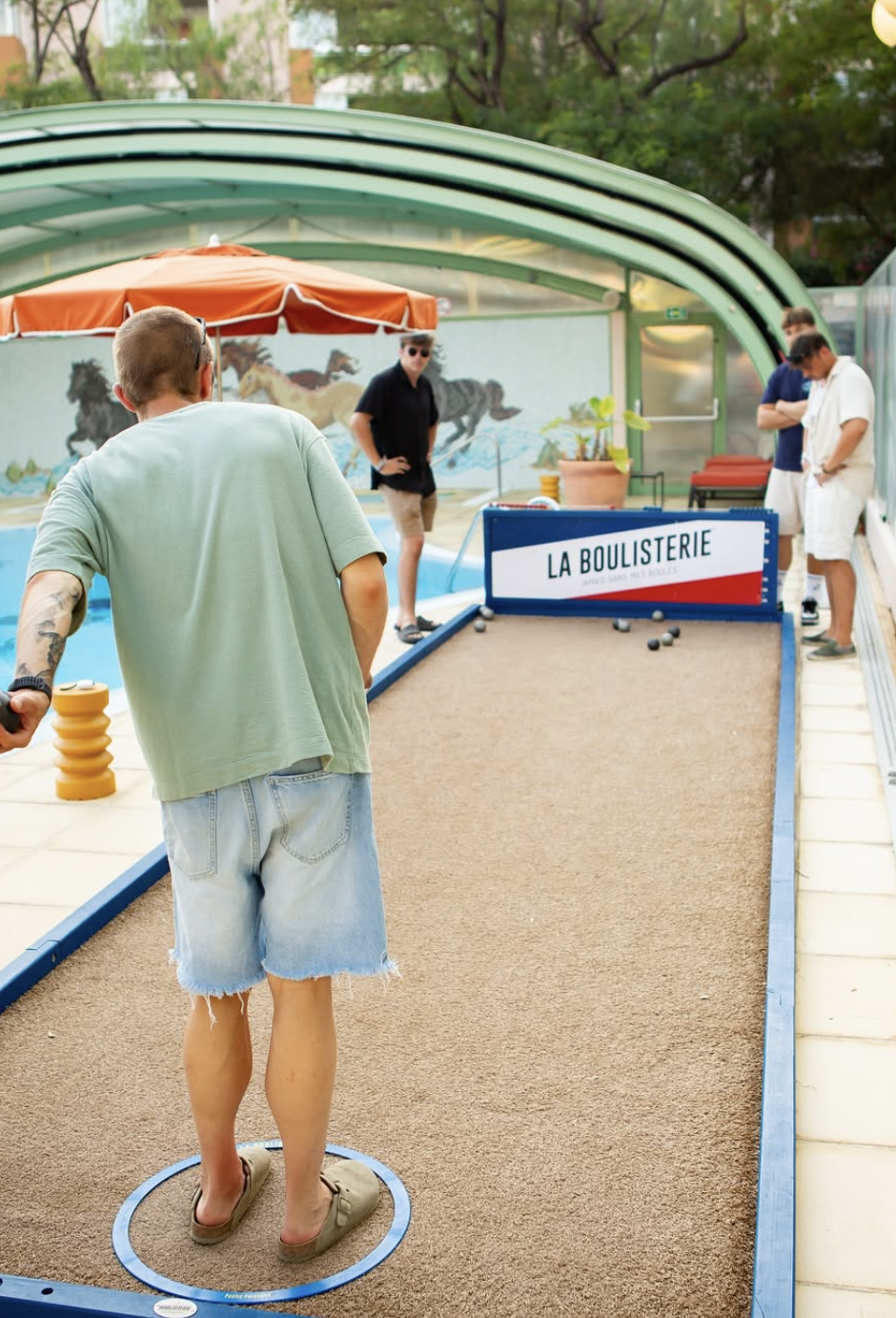 Personnes jouant à la pétanque dans une cour couverte, avec un panneau indiquant "La Boulisterie".