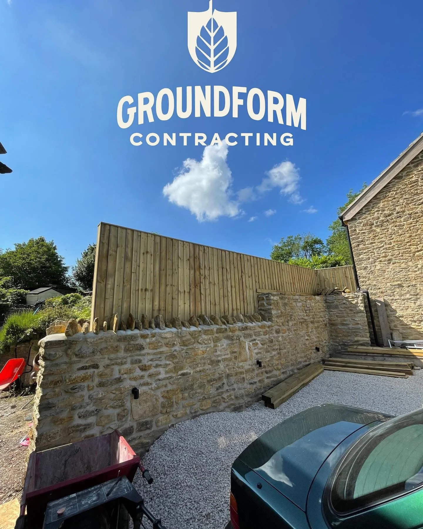 Construction site with stone wall and wooden fence under a bright blue sky with clouds, featuring the logo and text for Groundform Contracting.