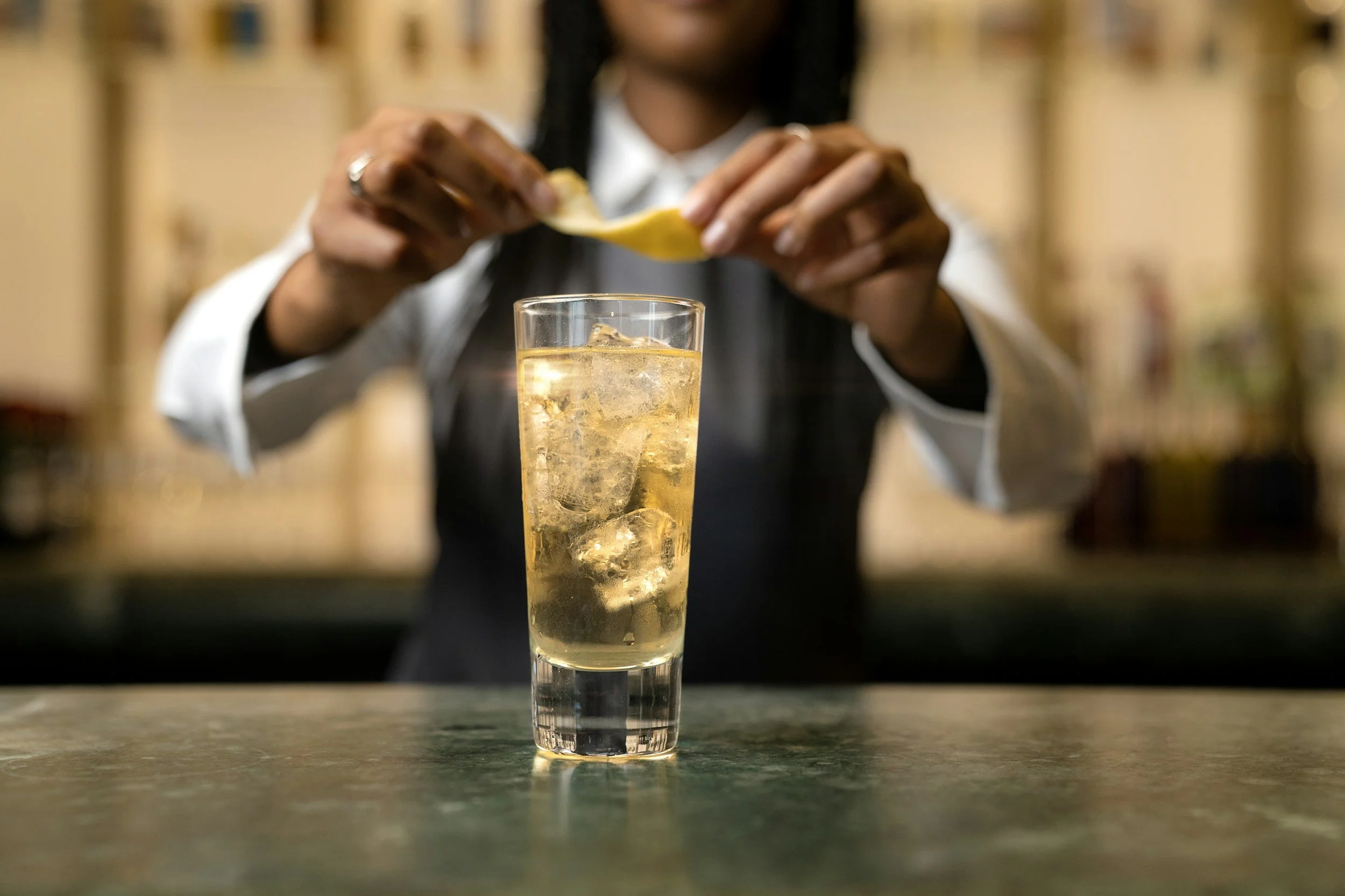 Barista squeezing lemon into a tall glass of iced beverage at a bar or cafe.