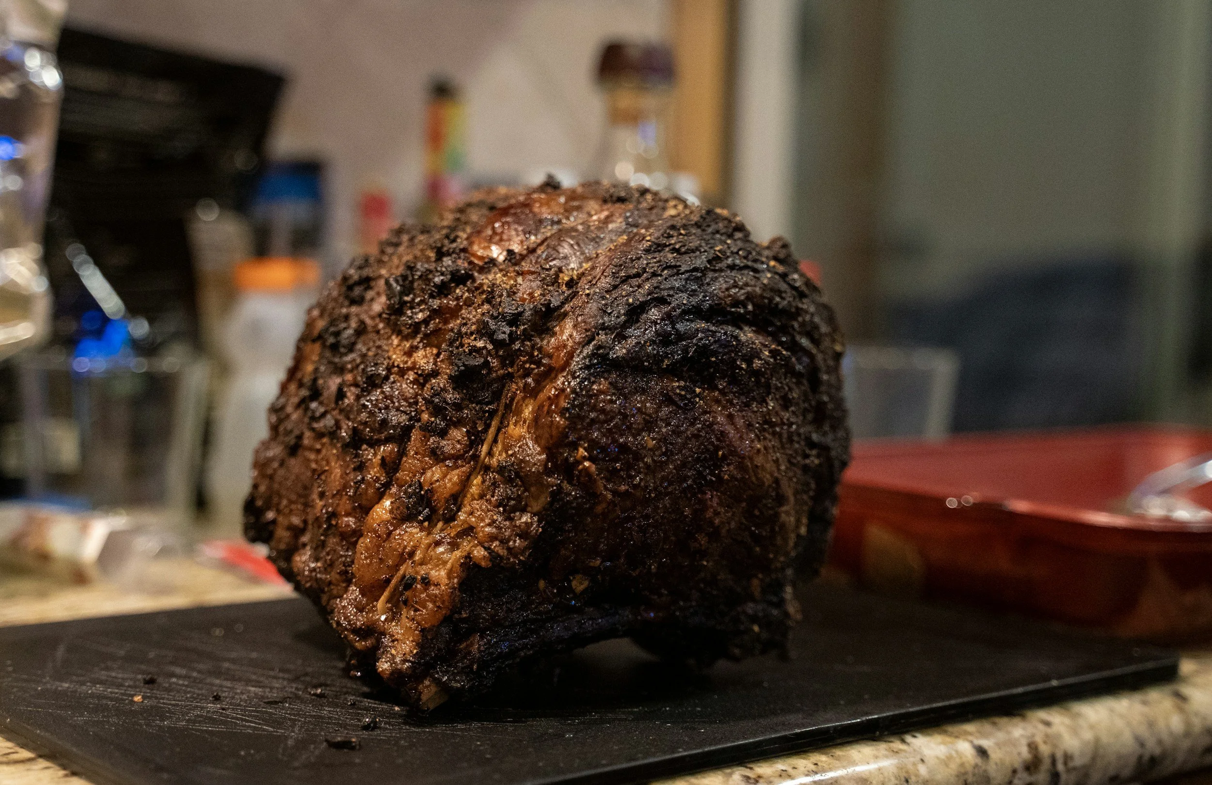 A smoked beef brisket with a dark, crispy bark resting on a black cutting board in a kitchen.