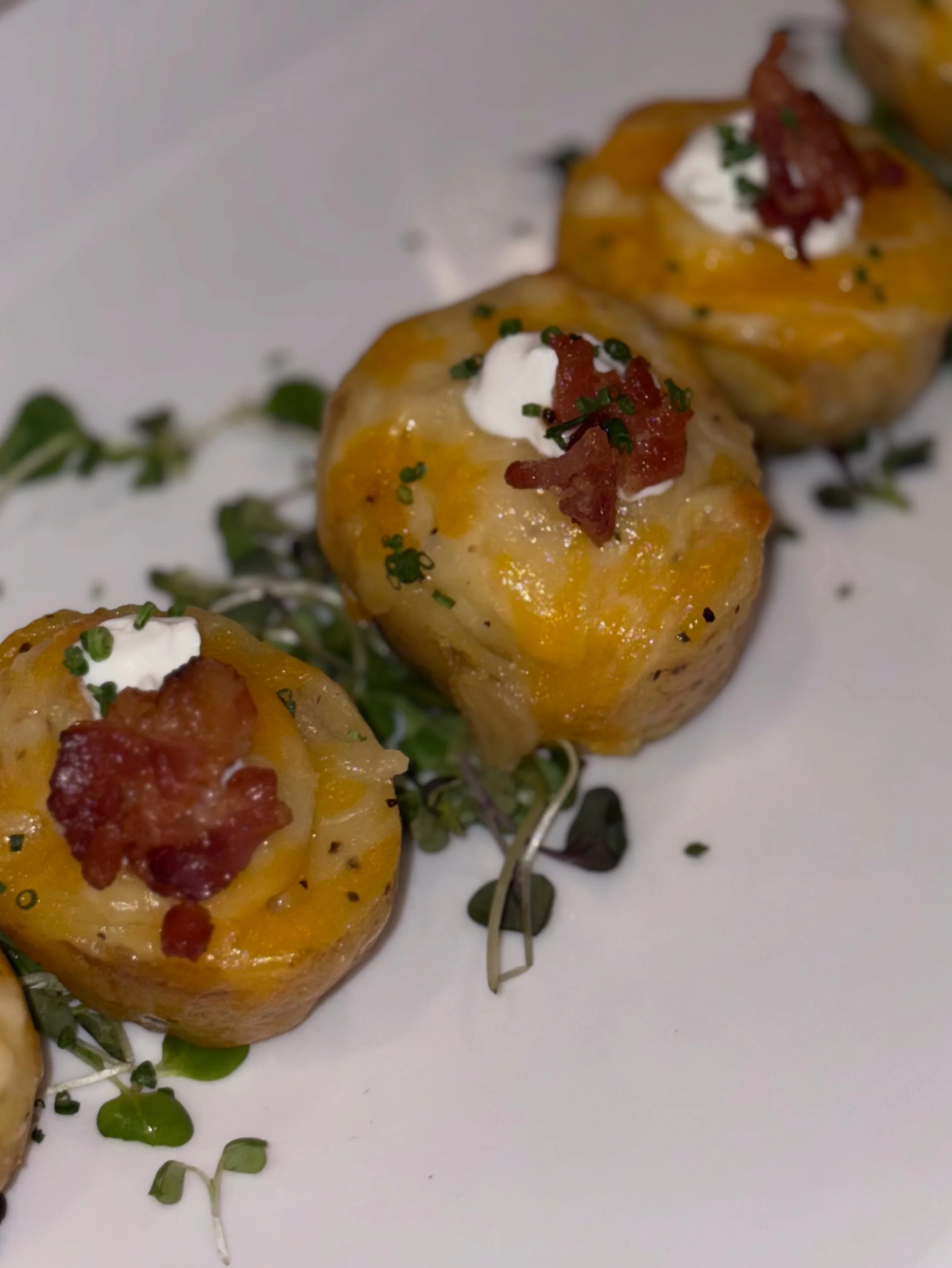 Close-up of four baked potato skins topped with cheese, sour cream, bacon bits, and chives on a white plate, garnished with microgreens.