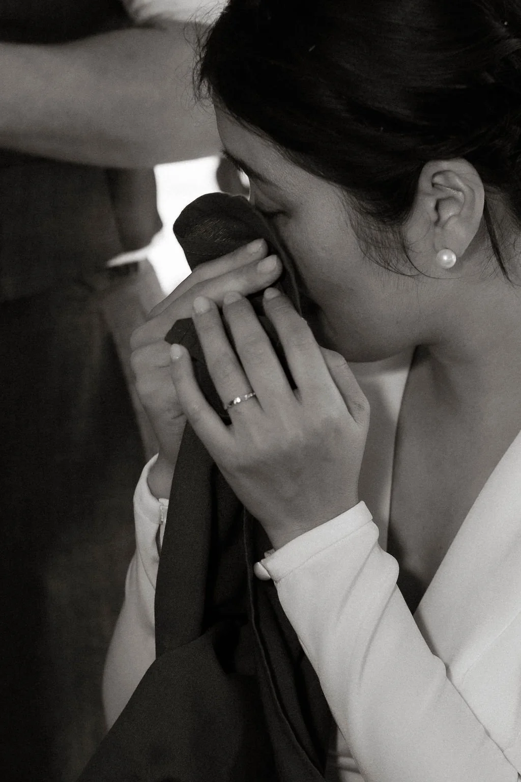 A woman with pearl earrings and a wedding ring kisses a microphone while holding it with both hands.