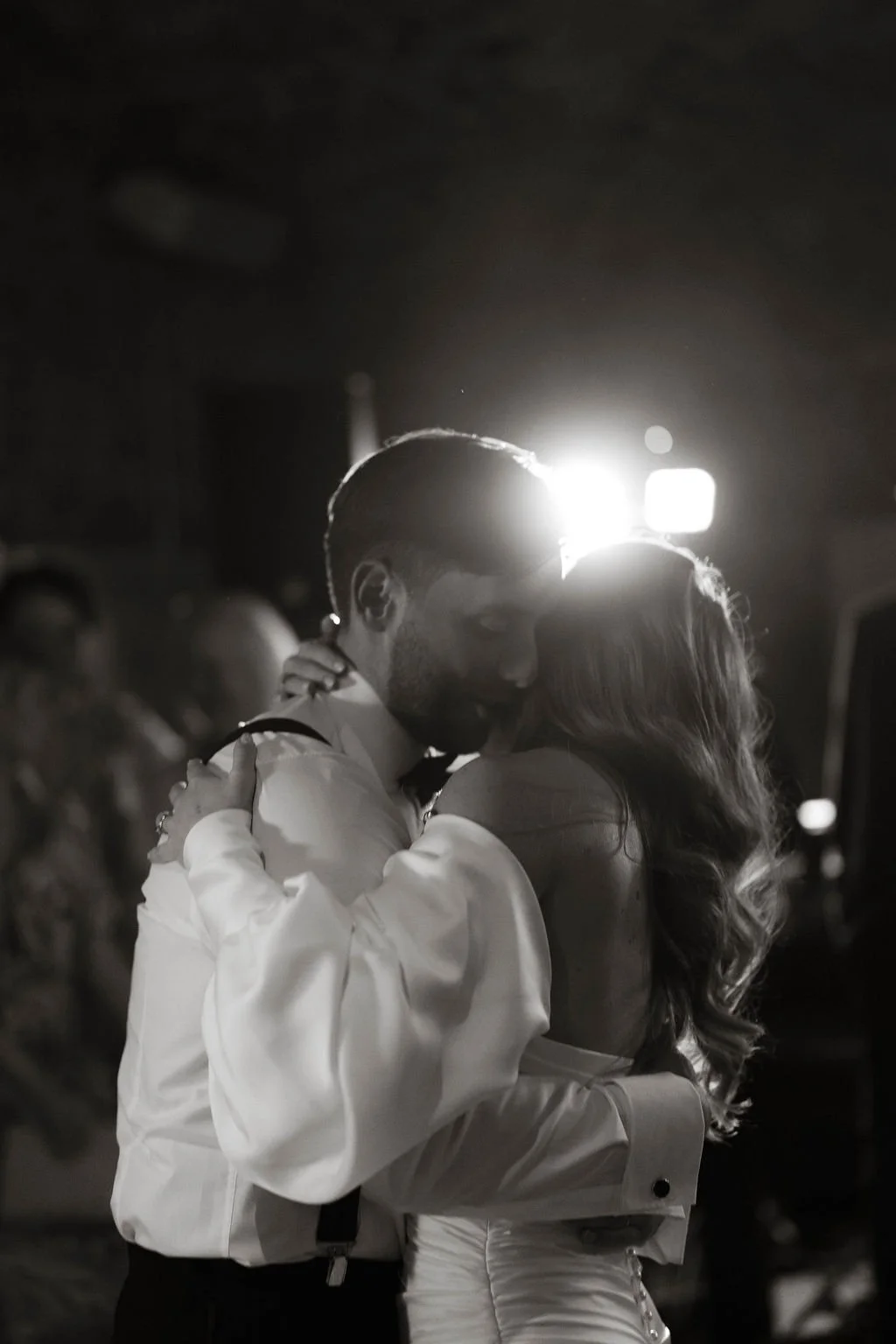 A black and white photo of a couple dancing closely, with their faces near each other, in a dimly lit setting.