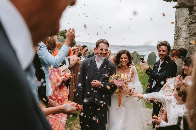 Happy bride and groom walking through a crowd of wedding guests as they throw confetti outdoors.