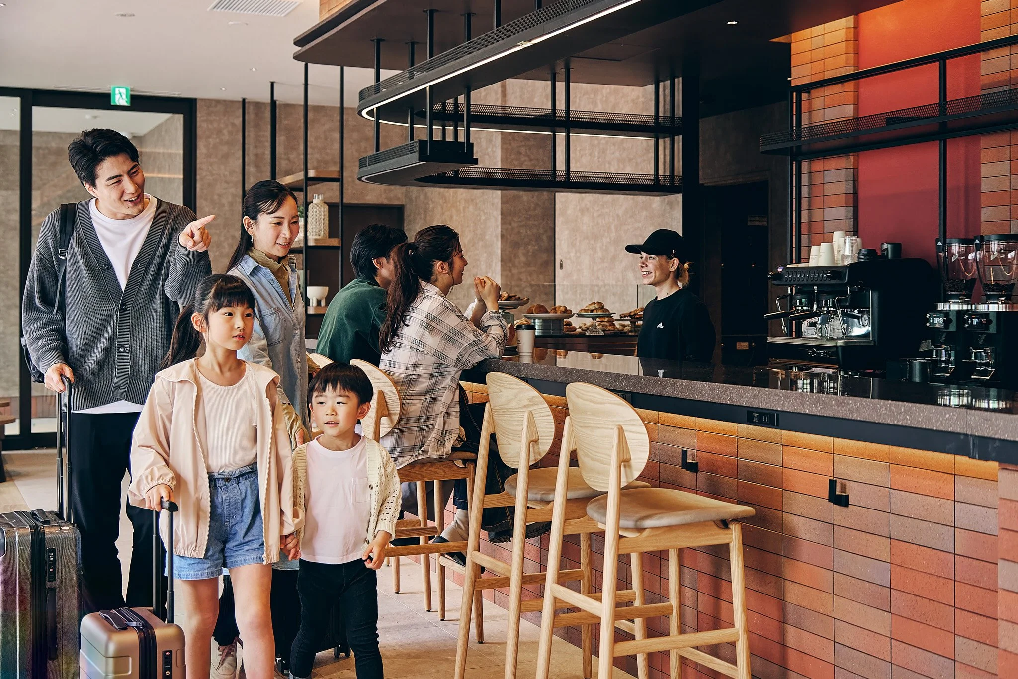 A family at a cafe counter ordering food with a barista serving.