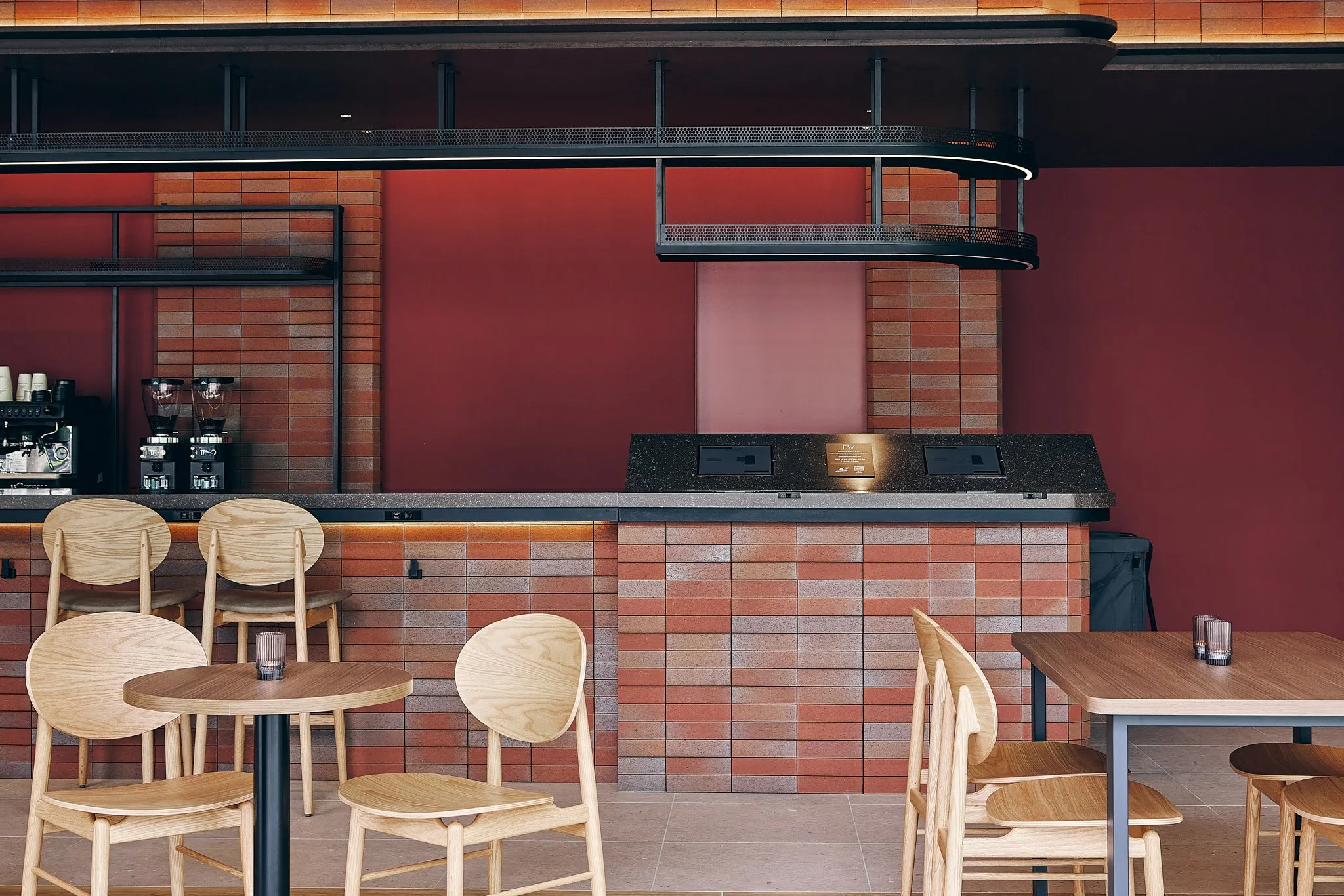 Interior of a modern coffee shop with wooden chairs and tables, brick walls, and an espresso machine on the counter.