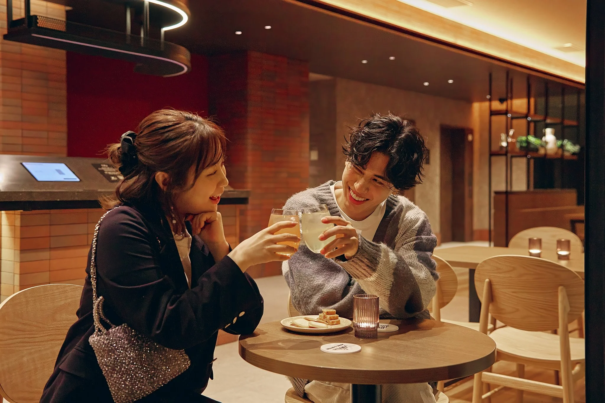 A man and woman sitting at a table in a restaurant, smiling, toasting with drinks, with dessert on the table.