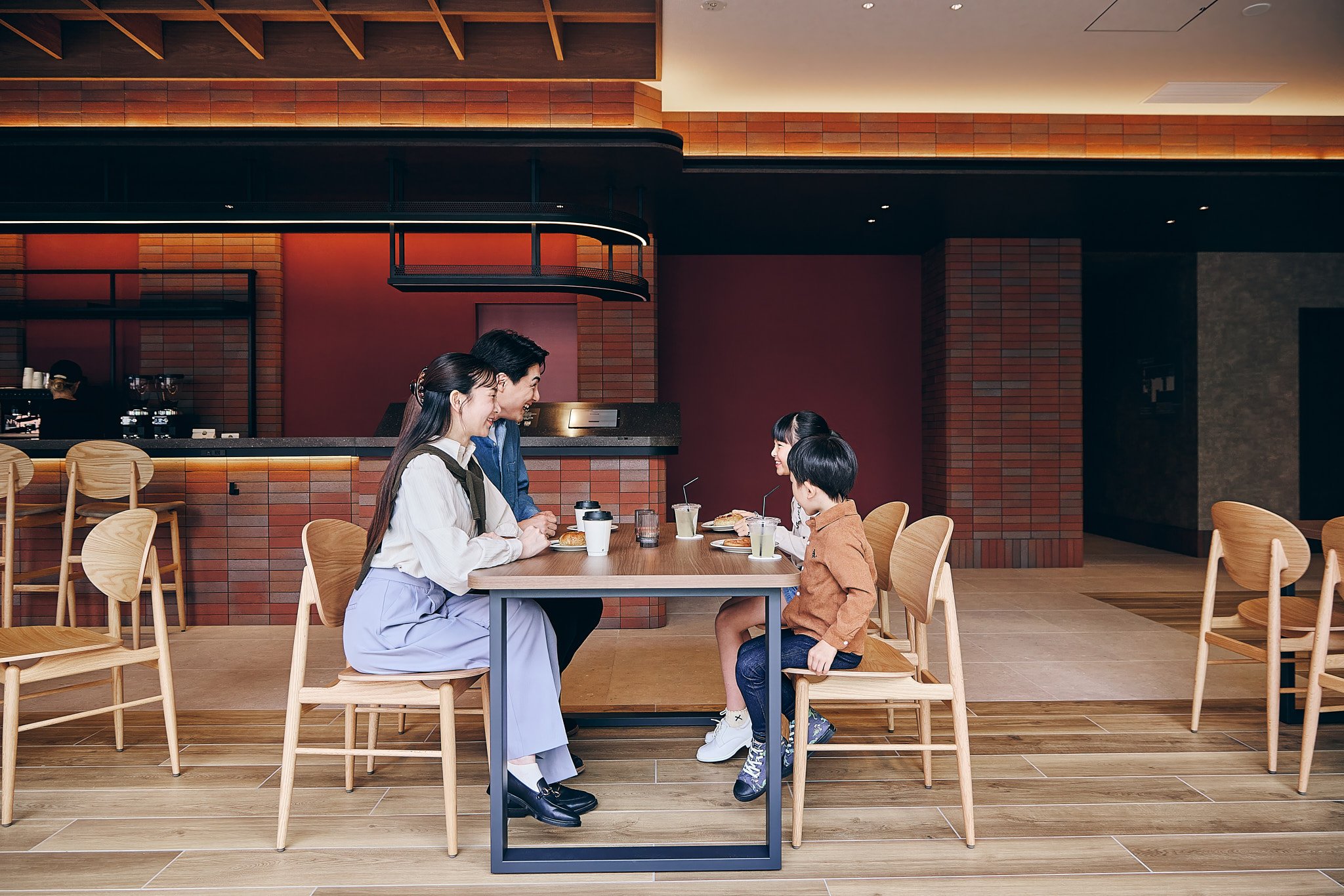 A woman and man sitting at a table with two children in a modern cafe, engaging in conversation with coffee and drinks on the table.