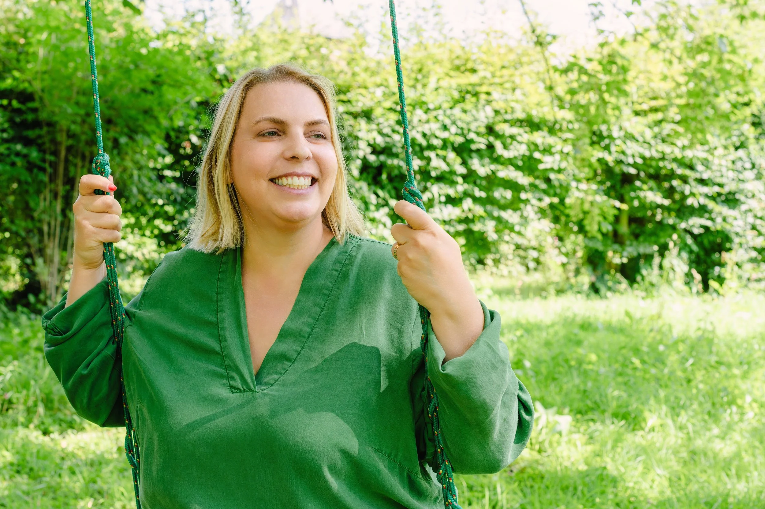 Elke Mertens, onafhankelijk archeologisch adviseur. Op de foto is ze herkenbaar als een vrouw die glimlacht terwijl ze op een schommel zit in een groene omgeving.