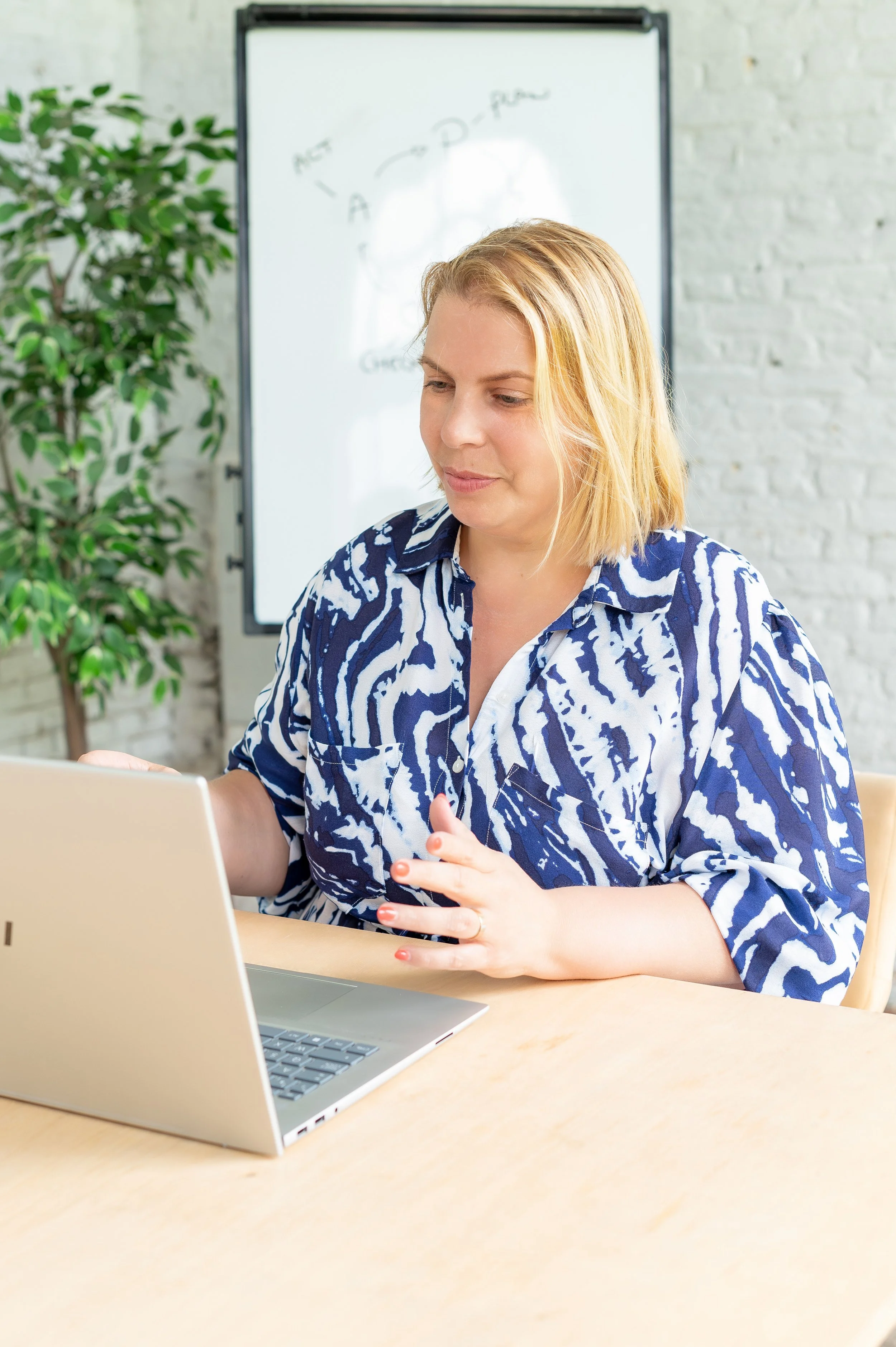 Elke Mertens, onafhankelijk archeologisch adviseur. Op de foto is ze herkenbaar als een vrouw die aan een laptop werkt in een kantoorruimte met een whiteboard en een plant op de achtergrond.