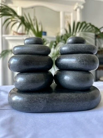 Two stacks of smooth, rounded black stones on a table with plants and a mirror in the background.