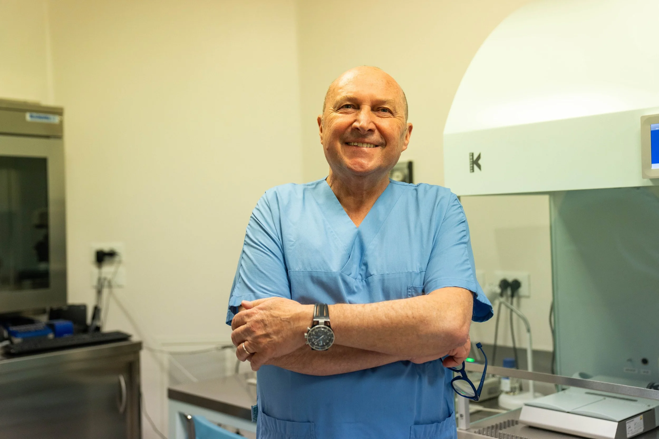 Medico sorridente in camice blu in un ambiente clinico.