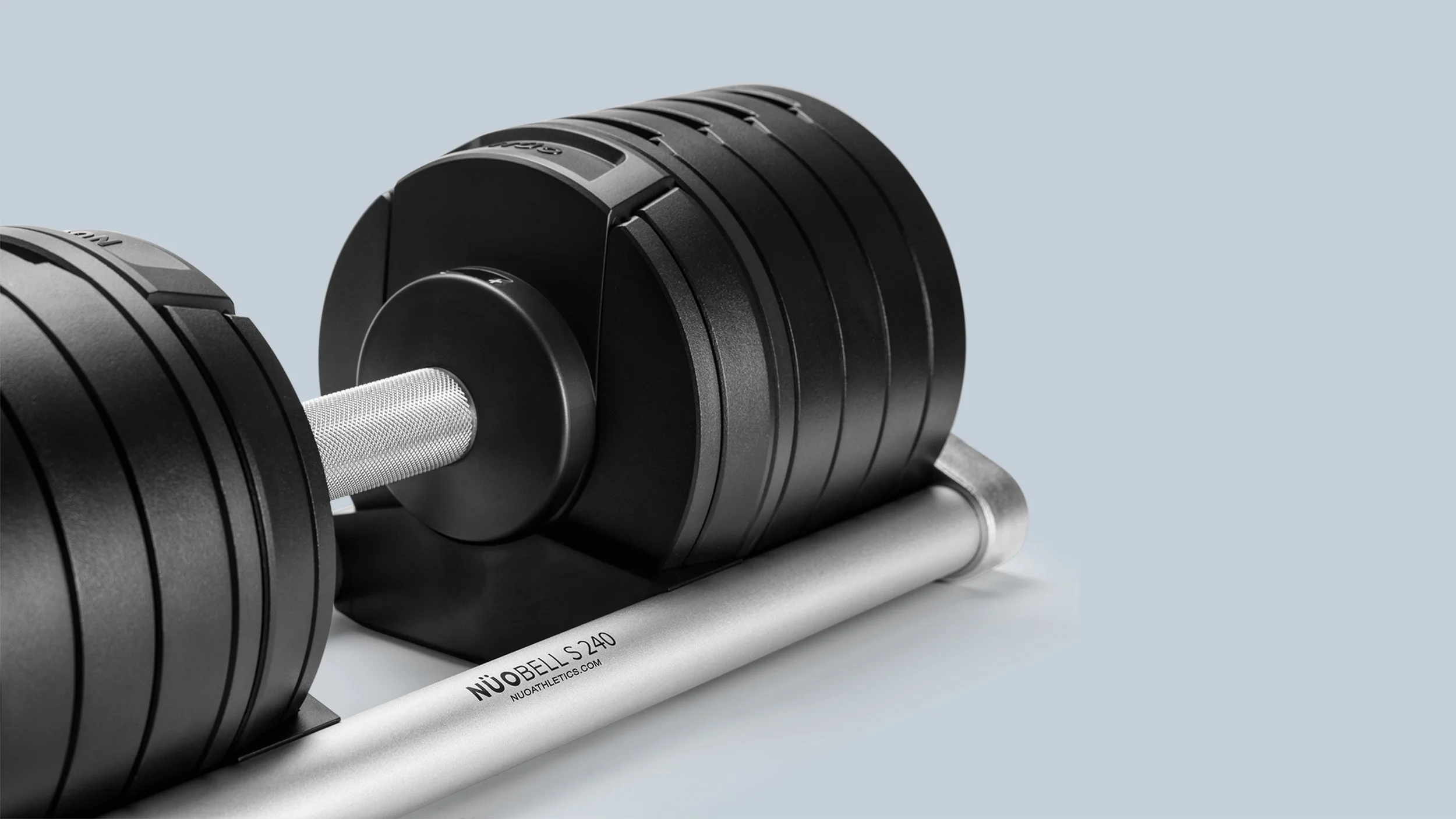 Close-up of a dumbbell with black weight plates on a gray rack against a light blue background.