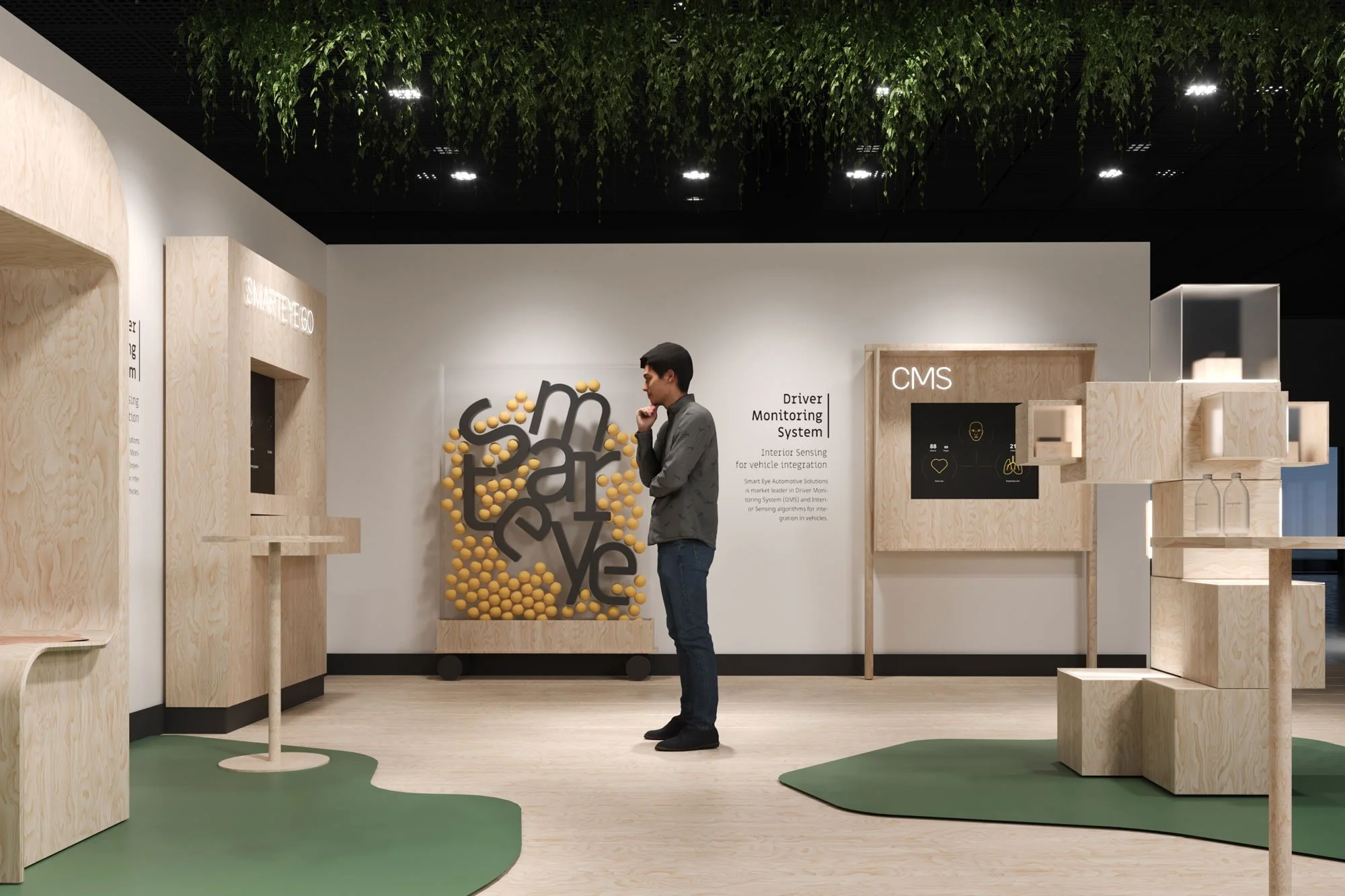 A man stands in a modern exhibition space with wooden display structures and a wall featuring a CMS system and informational text about vehicle monitoring systems.