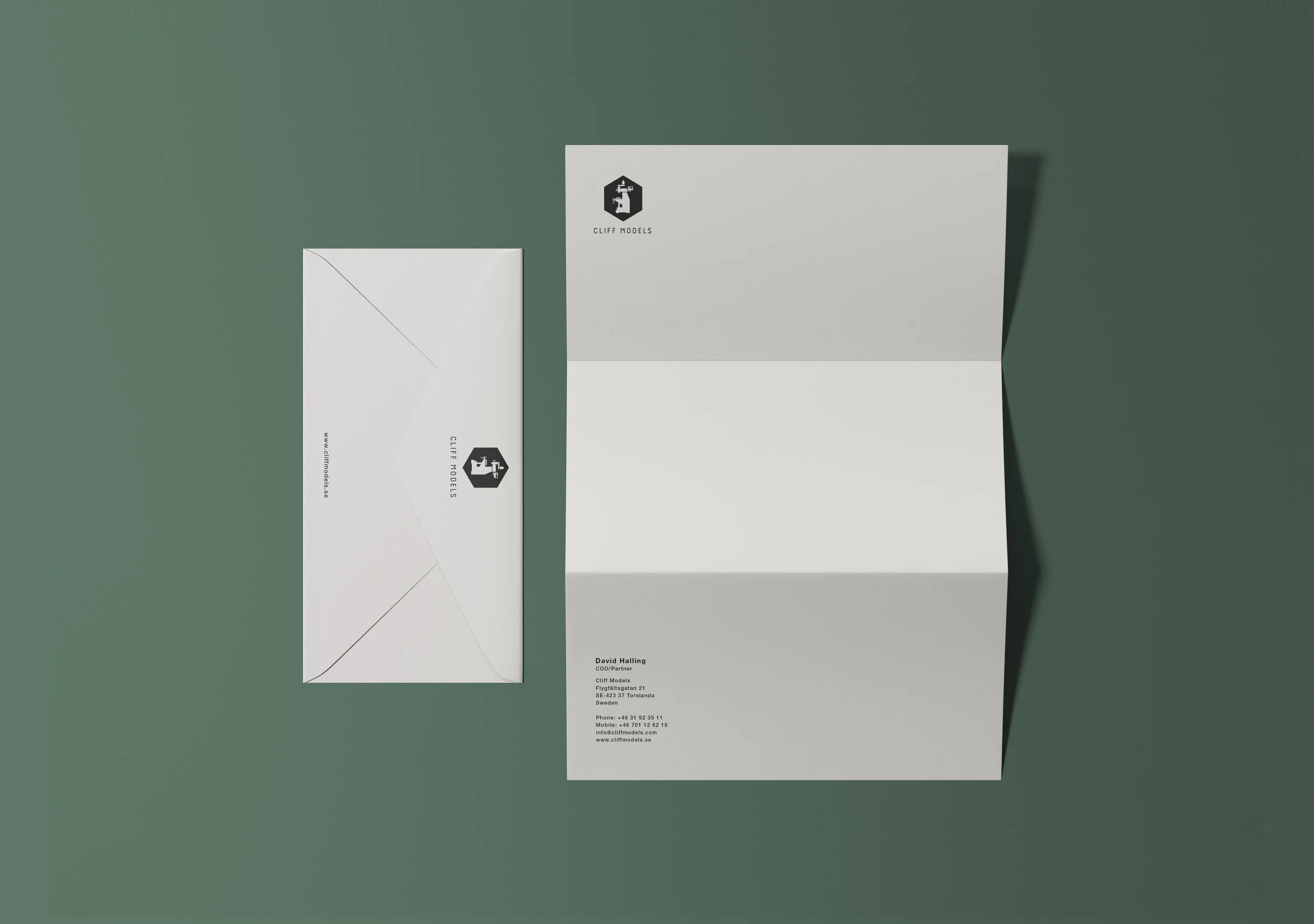 A white envelope and a folded white sheet with the logo and contact information of Cliff Models, placed on a green surface. The envelope has the logo on the seal flap, and the sheet displays the logo and contact details of David Halling.